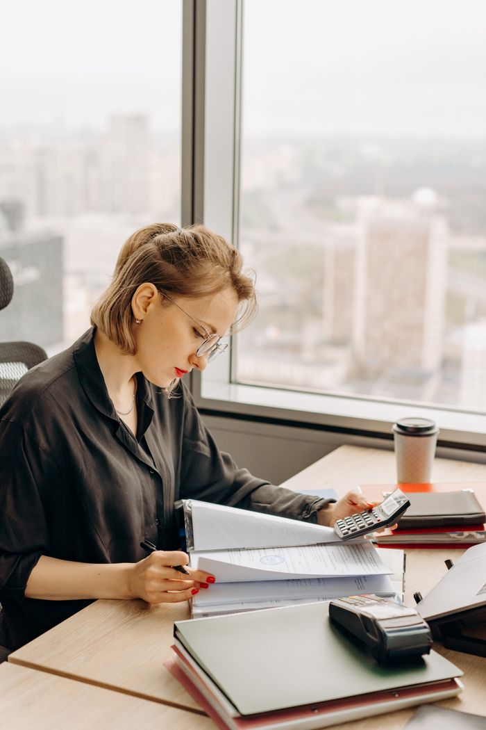Woman sitting at office desk reviewing financial documents with a calculator.